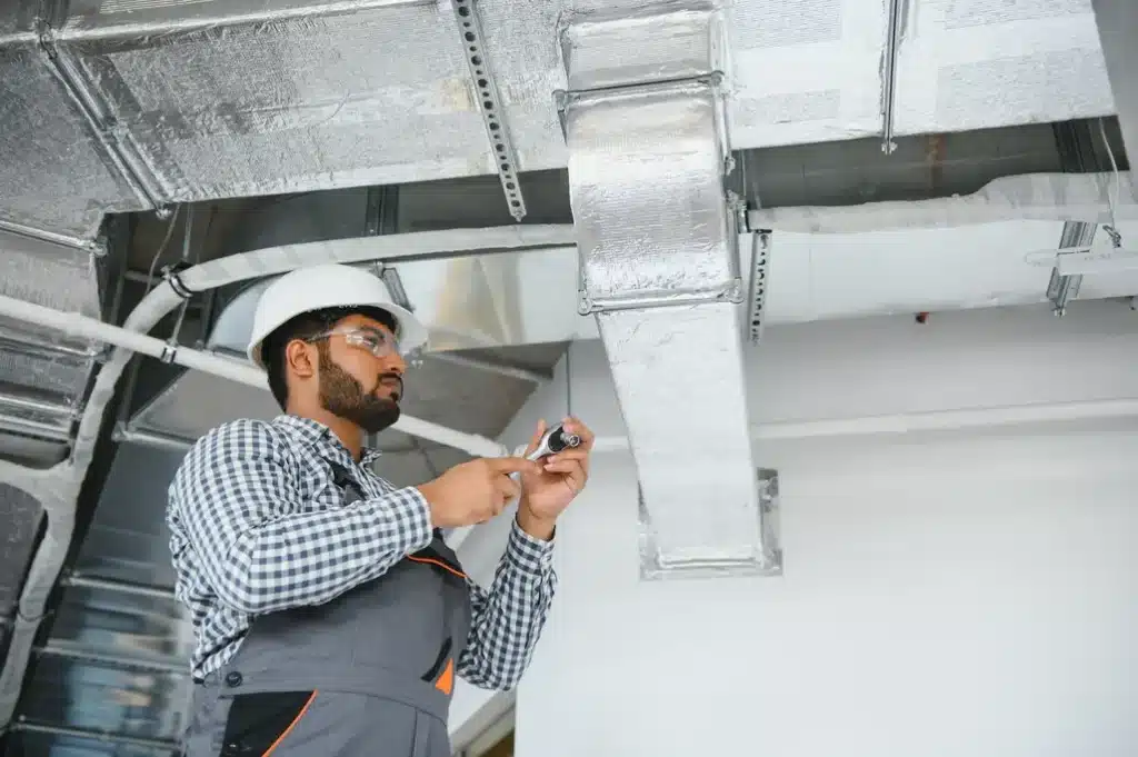HVAC technician inspecting air conditioning ductwork and ventilation system during AC maintenance.